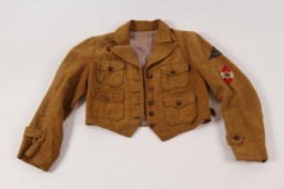 This League of German Girls jacket has two embroidered cloth patches handstitched to the upper left sleeve: a dark triangle displaying the name of the member’s region, South Franconia (Süd Franken), and a Hitler Youth insignia.
Beginning in 1933, the Hitler Youth and its organization for girls and young women, the League of German Girls, played an important role in the new Nazi regime. Through these organizations, the Nazi regime indoctrinated young people with Nazi ideology, including antisemitism and racism. All prospective members of the Hitler Youth had to be "Aryans" and "genetically healthy." Their duty was to serve Adolf Hitler and the Third Reich. Hitler Youth boys and girls were required to wear military-style uniforms, in keeping with the "soldierly" character of the Nazi Party, and conform to certain standards of behavior. Youth of both genders had to take part in physical exercise to prepare for their future lives in Nazi Germany. Boys engaged in military training, while the League of German Girls primed girls to be future wives and mothers. It trained girls to care for the home and family. Girls also learned skills such as sewing, nursing, cooking, and household chores.  
This jacket was brought back to the United States by Arthur R. Myers, a US Army soldier who participated in the Allied invasion of Nazi Germany.