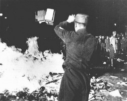 At Berlin's Opernplatz (Opera Square), an SA man throws books into the flames at the public burning of books deemed "un-German." This image is a still from a motion picture. Berlin, Germany, May 10, 1933.