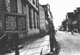 Tábla német és lett felirattal, amely arra figyelmeztet, hogy a kerítést átlépő vagy a rigai gettó lakóival kapcsolatot létesítő személyeket lelövik. Riga, Lettország, 1941–1943.