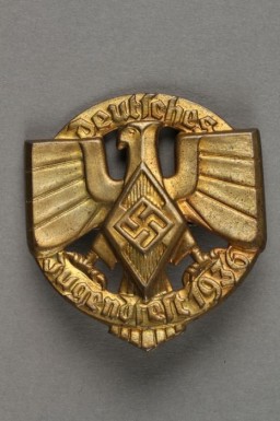 This badge shows the Hitler Youth insignia and Nazi German national symbol superimposed over ring bearing the raised text, "Deutsches/Jugendfest 1936."
Beginning in 1933, the Hitler Youth and the League of German Girls had an important role to play in the new Nazi regime. Through these organizations, the Nazi regime planned to indoctrinate young people with Nazi ideology. This was part of the process of Nazifying German society. The aim of this process was to dismantle existing social structures and traditions. The Nazi youth groups were about imposing conformity. Youth throughout Germany wore the same uniforms, sang the same Nazi songs, and participated in similar activities. Badges such as this one helped foster indoctrination and uniformity.  