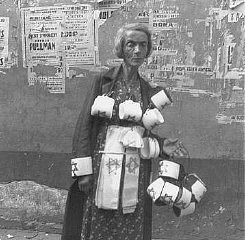 Une femme décharnée vend des brassards frappés de l’étoile jaune dont le port était obligatoire pour les Juifs. A l’arrière plan, il y a des affiches de concerts ; presque toutes sont détruites. Ghetto de Varsovie, Pologne, 19 septembre 1941.