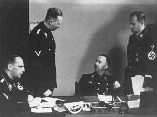 Heinrich Himmler (seated, center), chief of the SS, with Reinhard Heydrich (standing, left), chief of the Reich Main Security Office ...