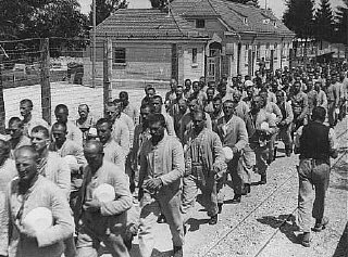 Para tahanan tengah membawa mangkuk di kamp konsentrasi Dachau.