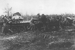 一德军纵队在泥浆里奋力前进，路过一辆毁坏的苏联坦克。