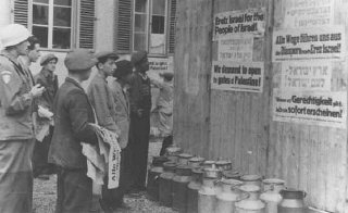 Jewish survivors in a displaced persons camp post signs calling for Great Britain to open the gates of Palestine to the Jews.